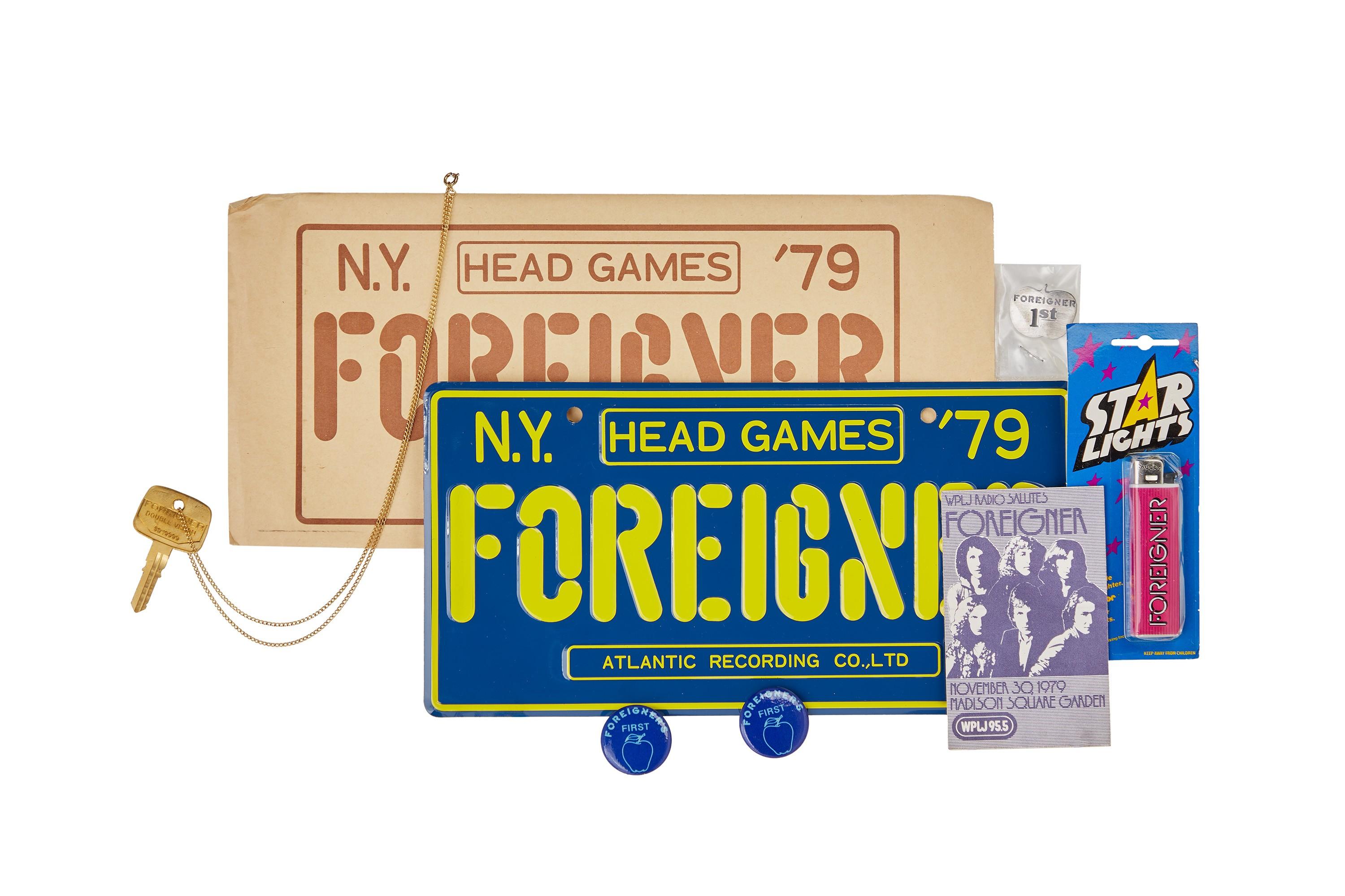Foreigner | Vintage Memorabilia A collection of Foreigner "Head Games '79" merchandise, including a blue and yellow New York license plate, a tan sign, a key, a band flyer, and a pink lighter.