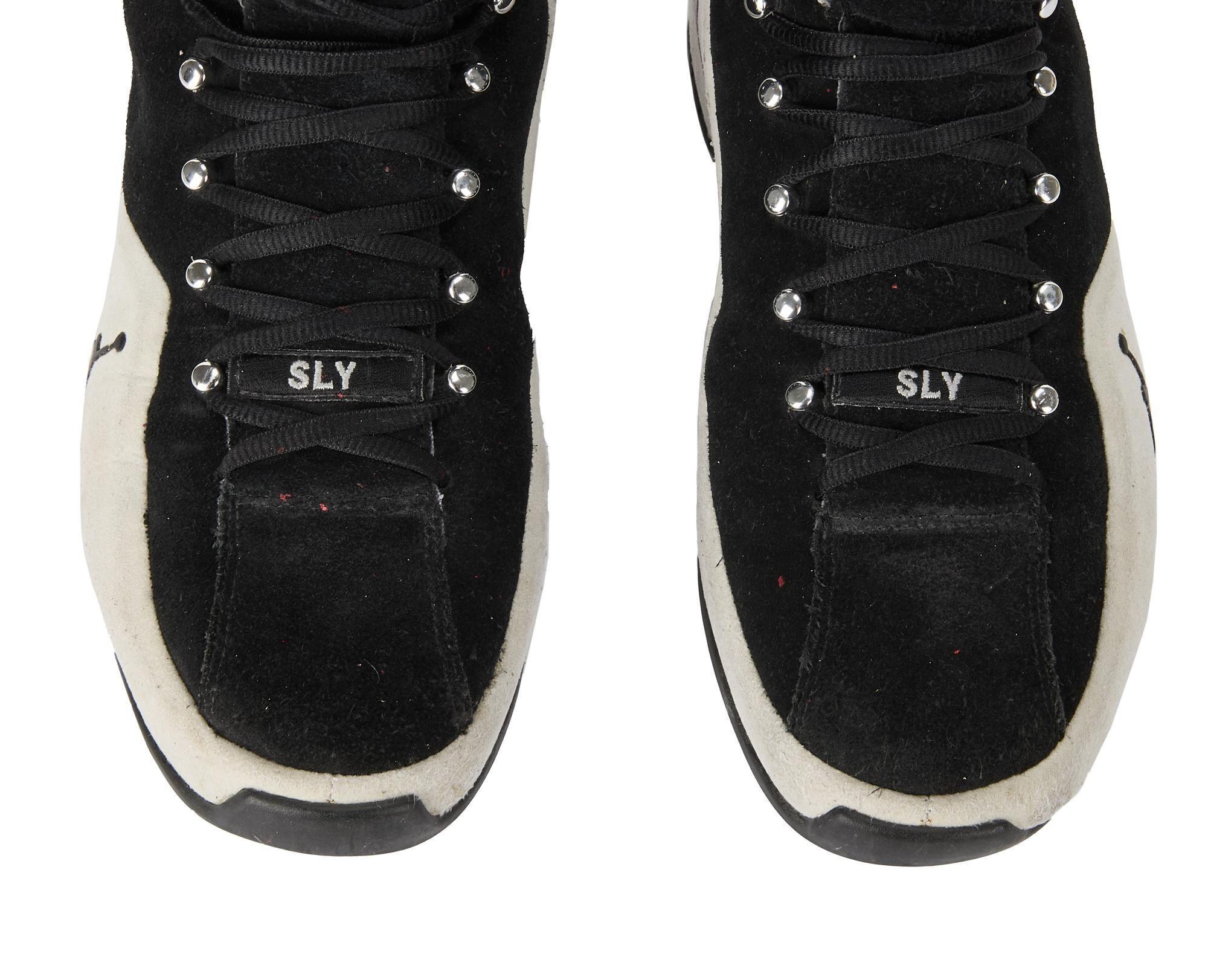 a pair of black and white sneakers with the word sly on the laces .