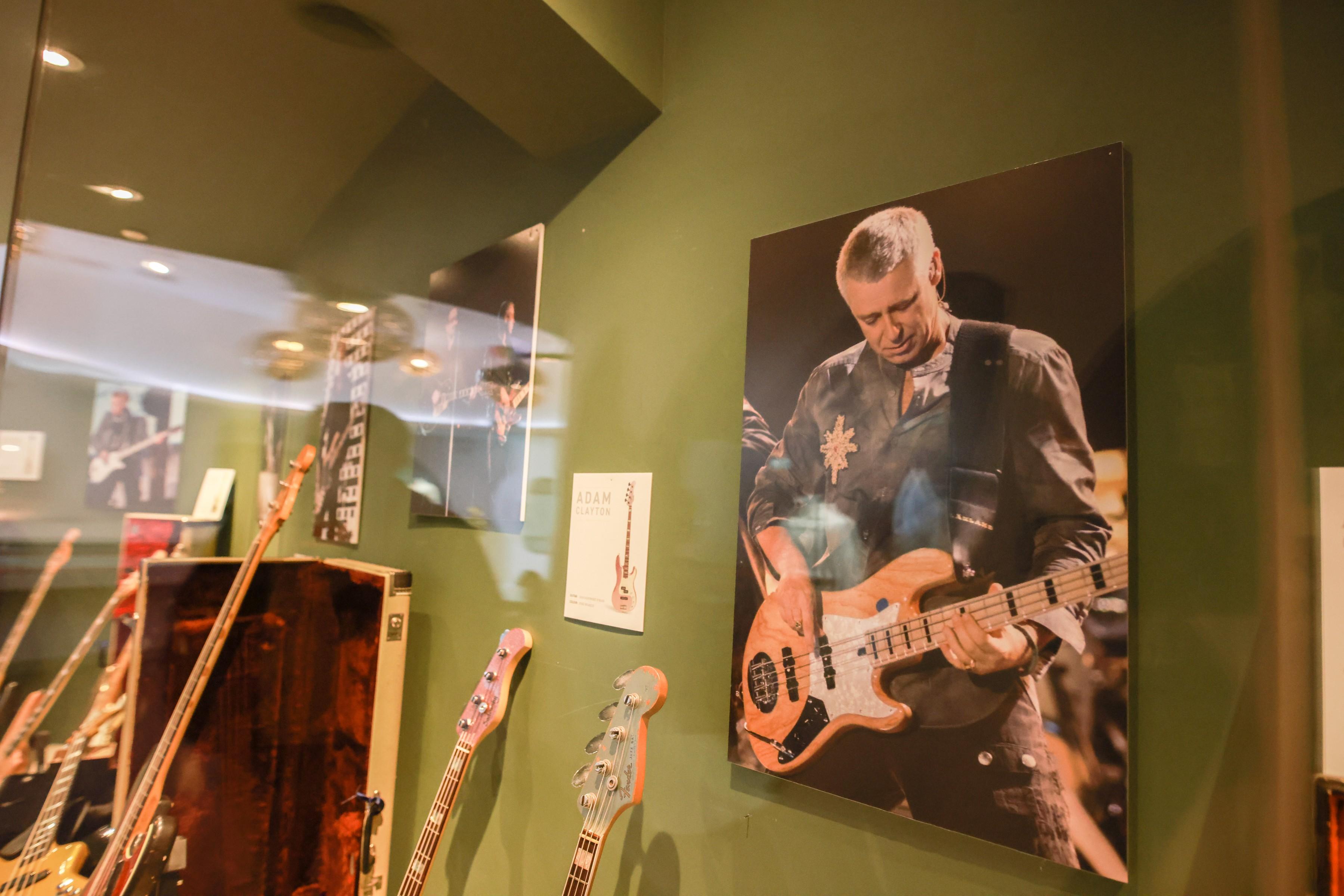 a performance photo of adam clayton playing one of his guitars that julien's is auctioning 