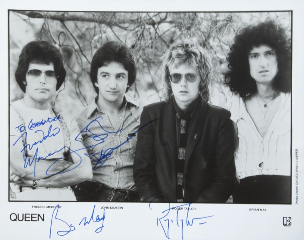 a black and white photo of the queen band signed by all four members .