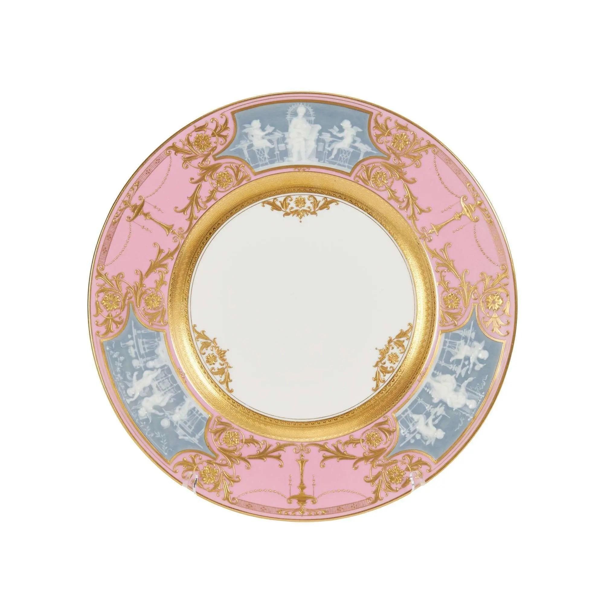 Lot #299. Whoopi Goldberg | Set of 12 Mintons Pate-sur-Pate Dinner Plates A round decorative plate with a pink and light blue rim featuring gold baroque patterns and white classical figures, surrounding a white center.