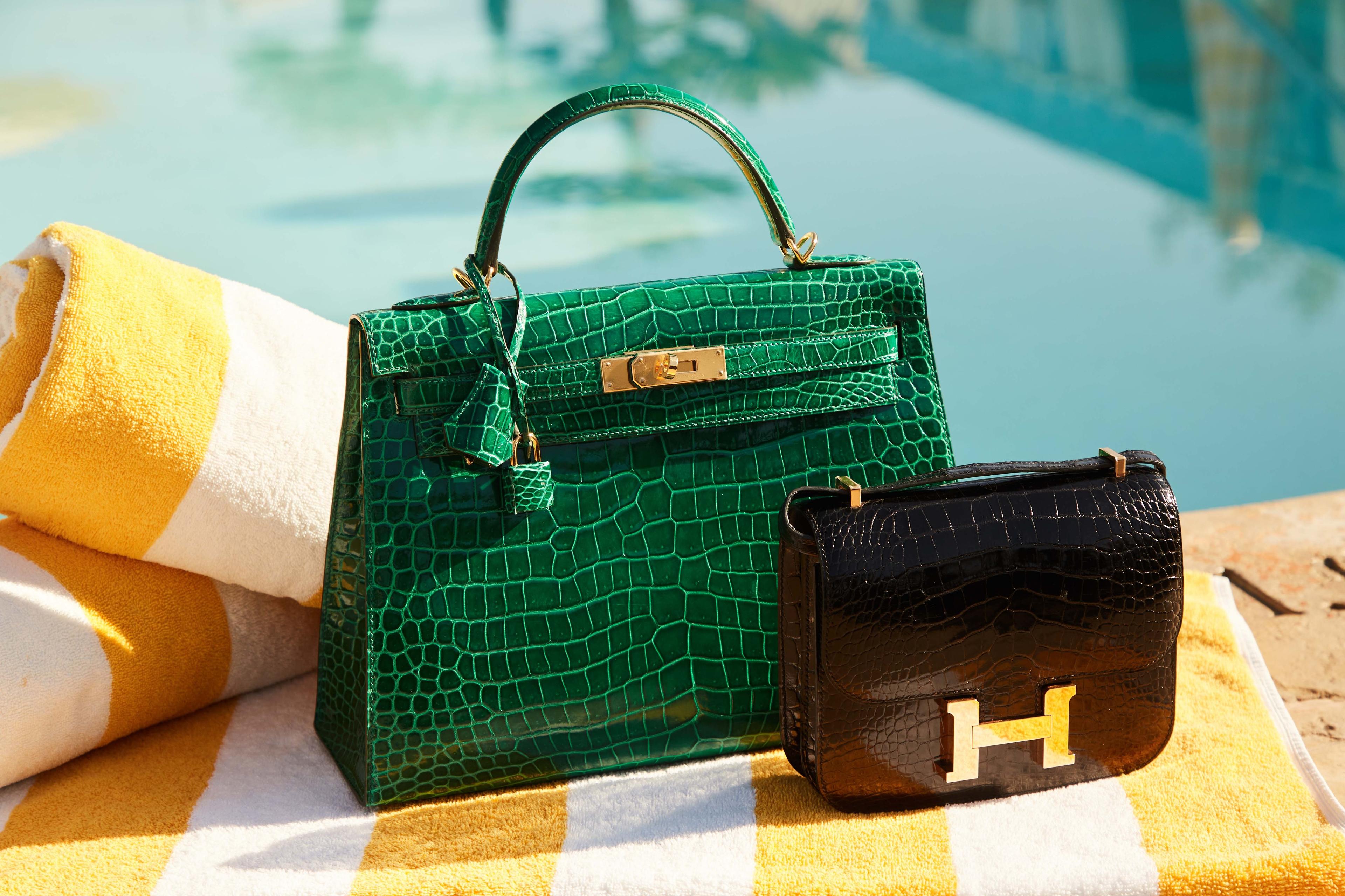 a green purse and a black purse are sitting on a striped towel next to a pool .