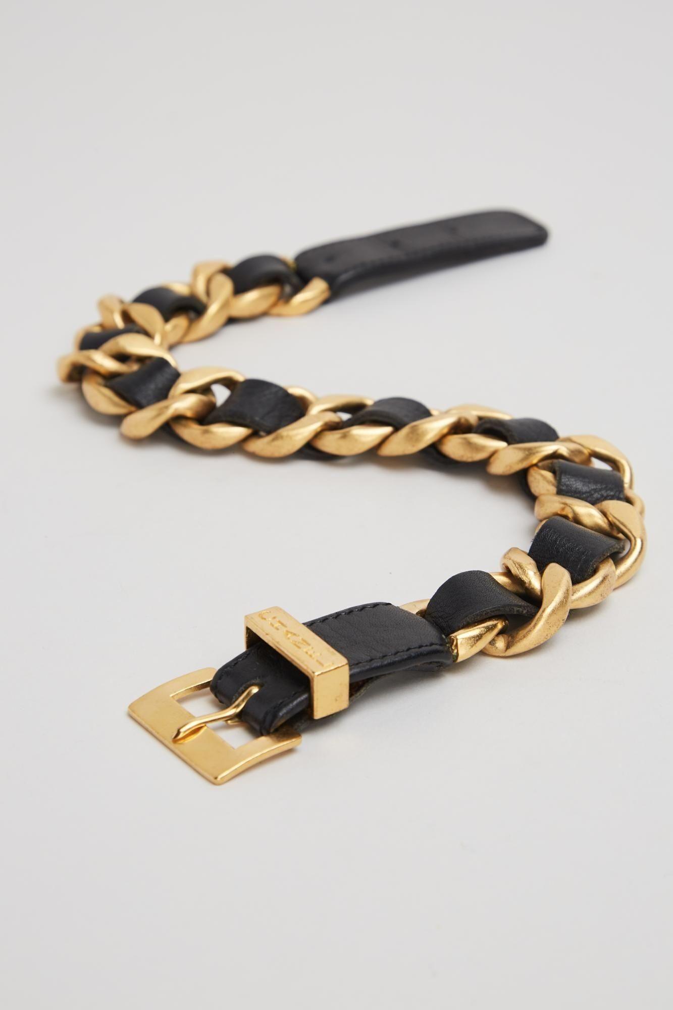 a black leather belt with gold chains and a gold buckle .
