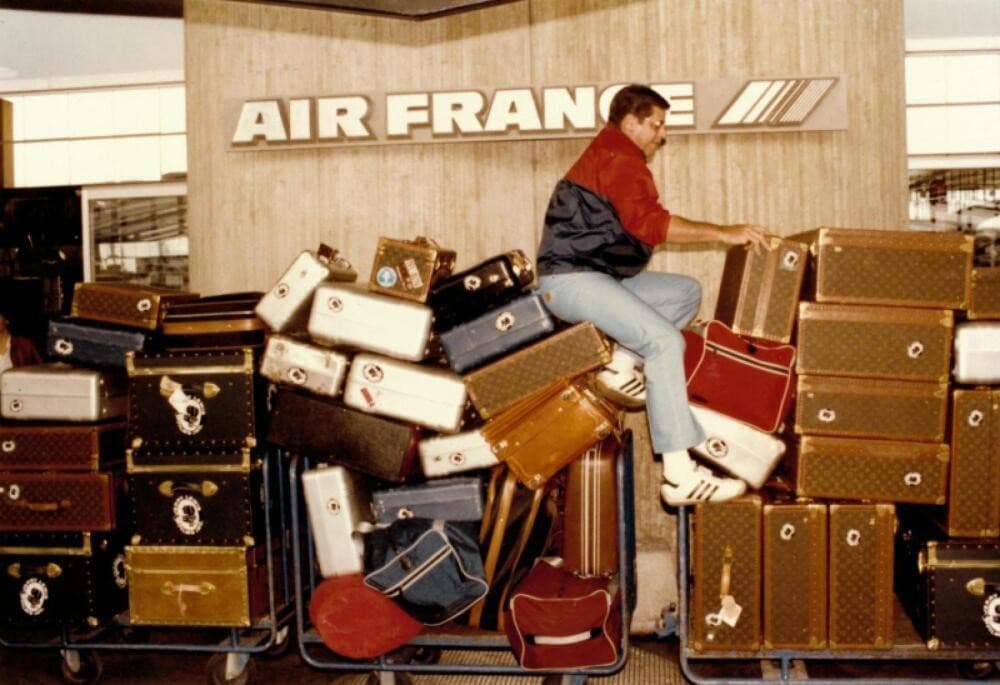 a man is sitting on top of a cart filled with luggage in front of an air france sign .