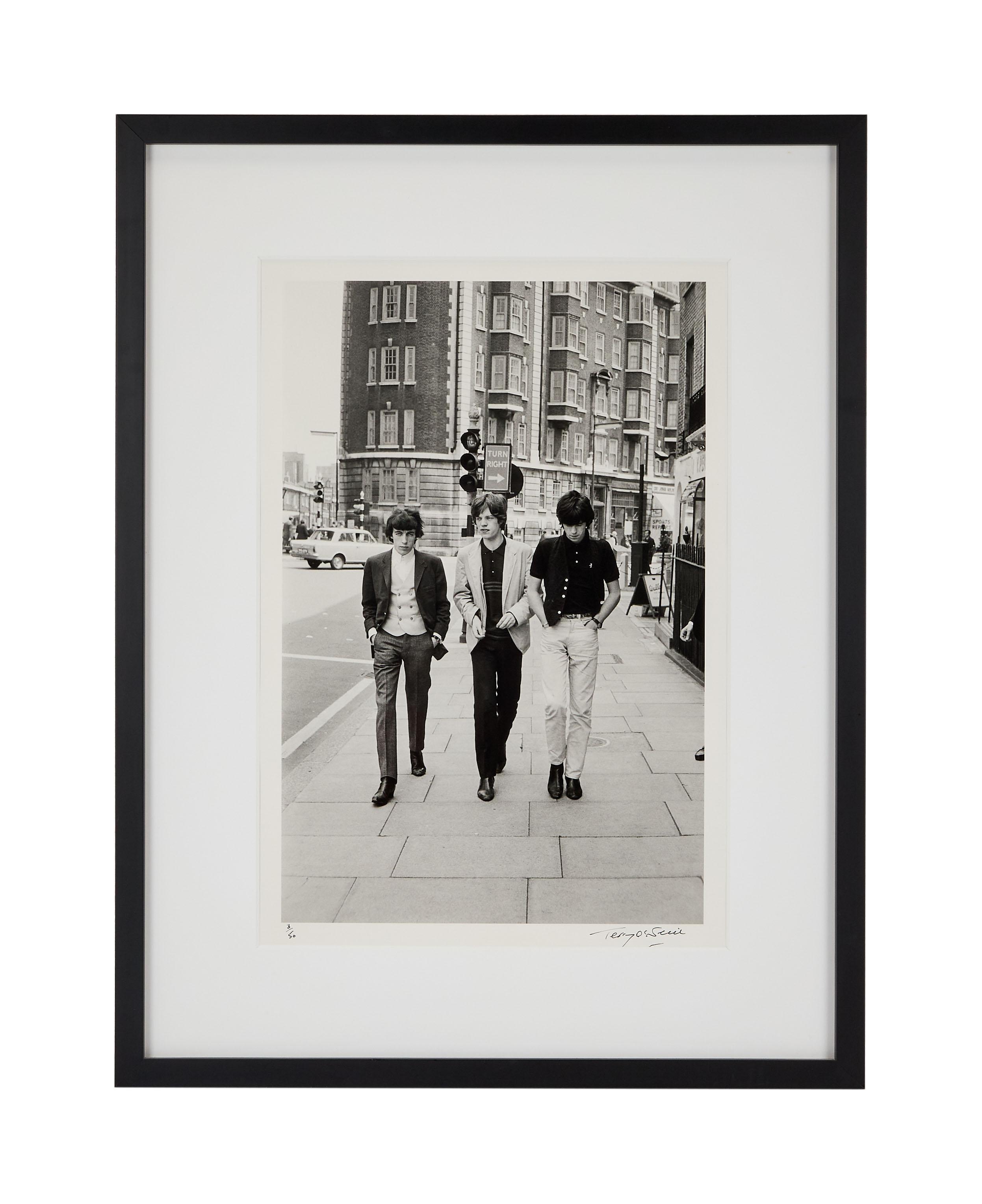 Lot #92. Paul Oakenfold | Rolling Stones 1963 Photo by Terry O'Neill a black and white photo of the rolling stones walking down a sidewalk .