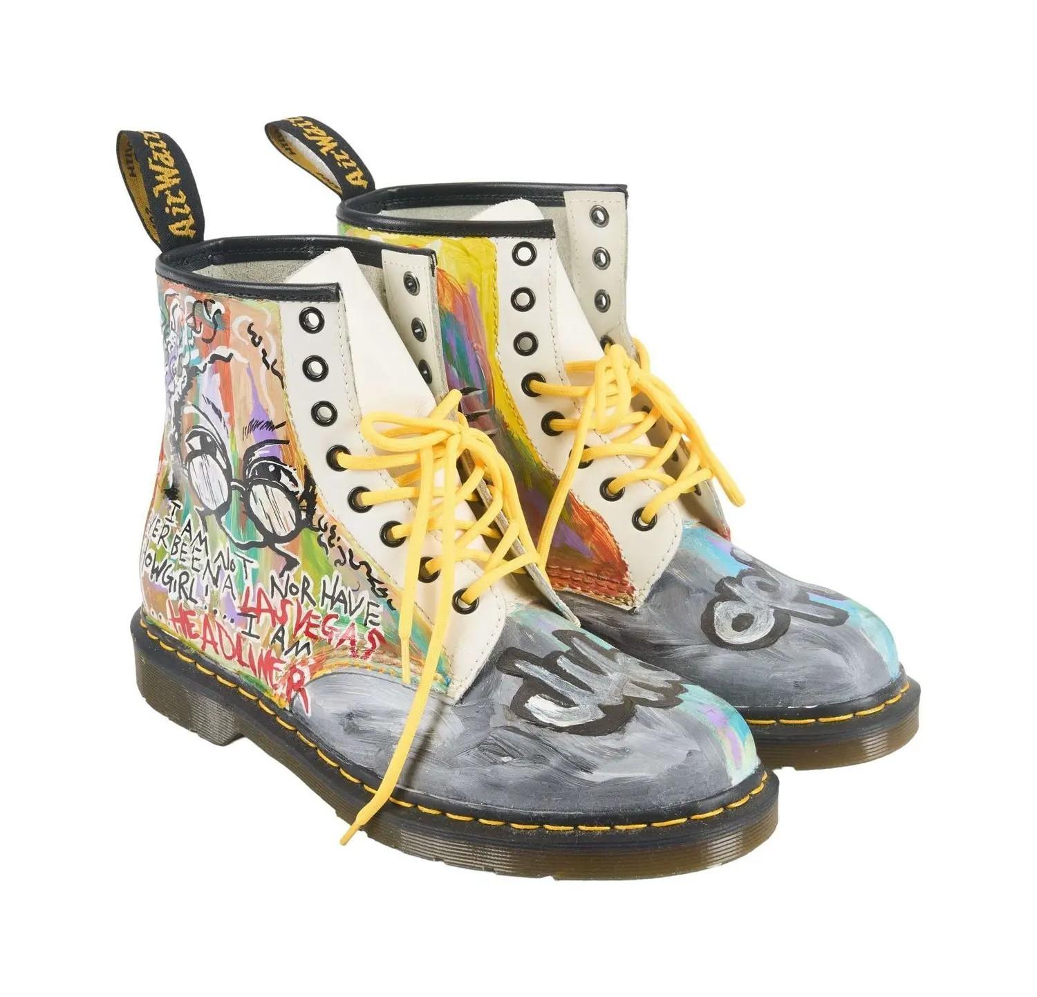 A pair of cream Doc Martens boots covered in vibrant, graffiti-style hand-painted artwork, with yellow laces.