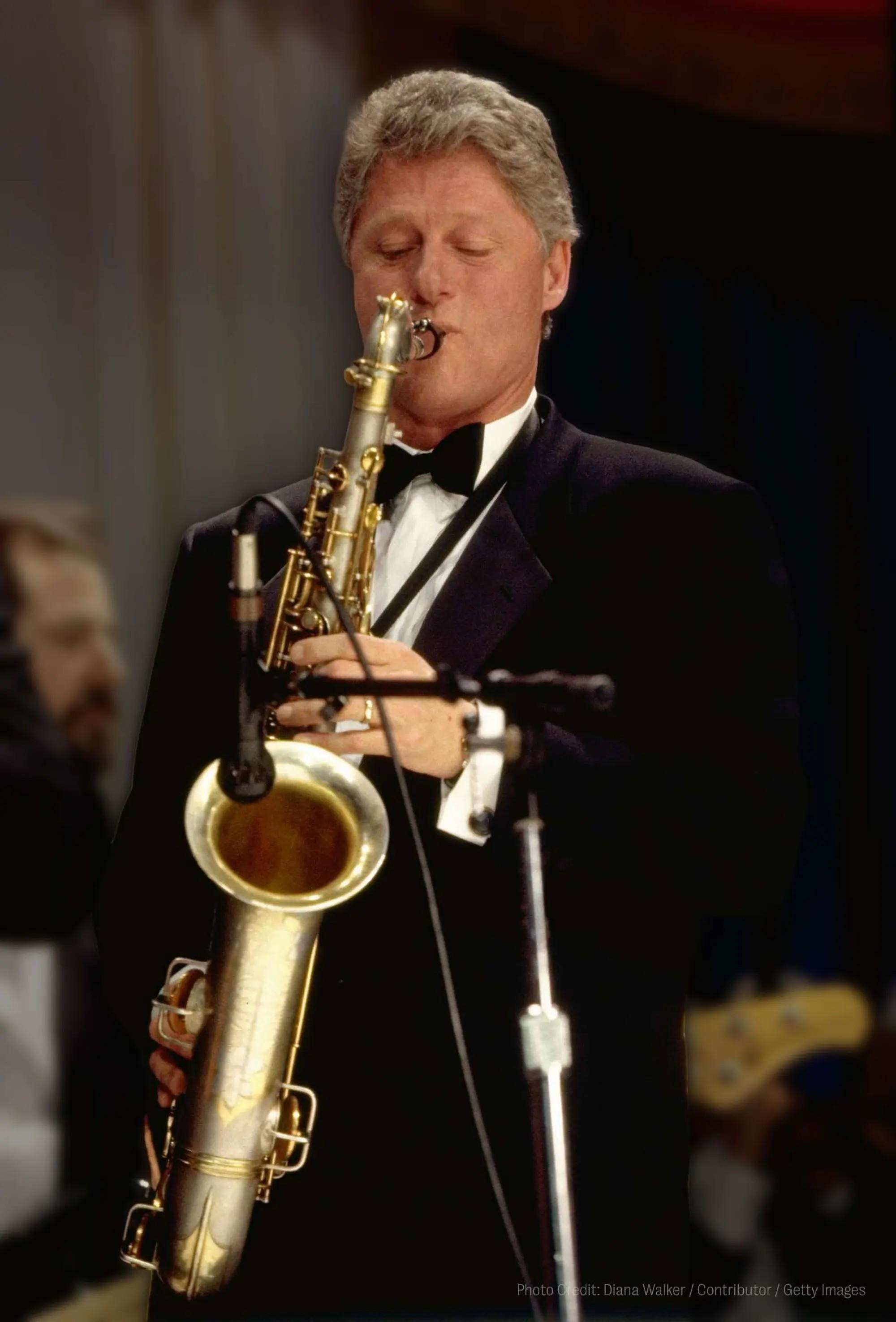 Bill Clinton playing the saxophone while wearing a tuxedo with his eyes closed.