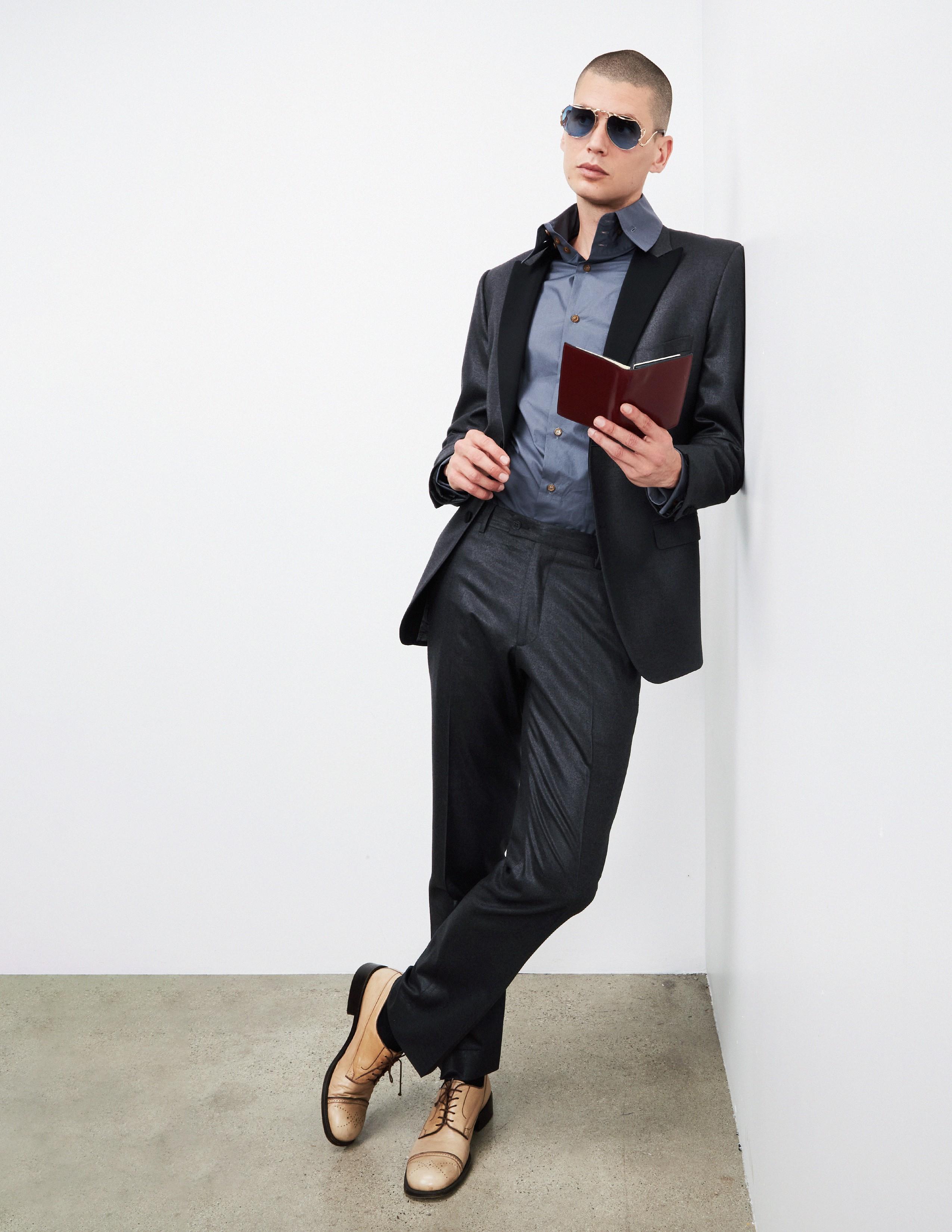 a man wearing a suit while leaning against a wall and holding a book