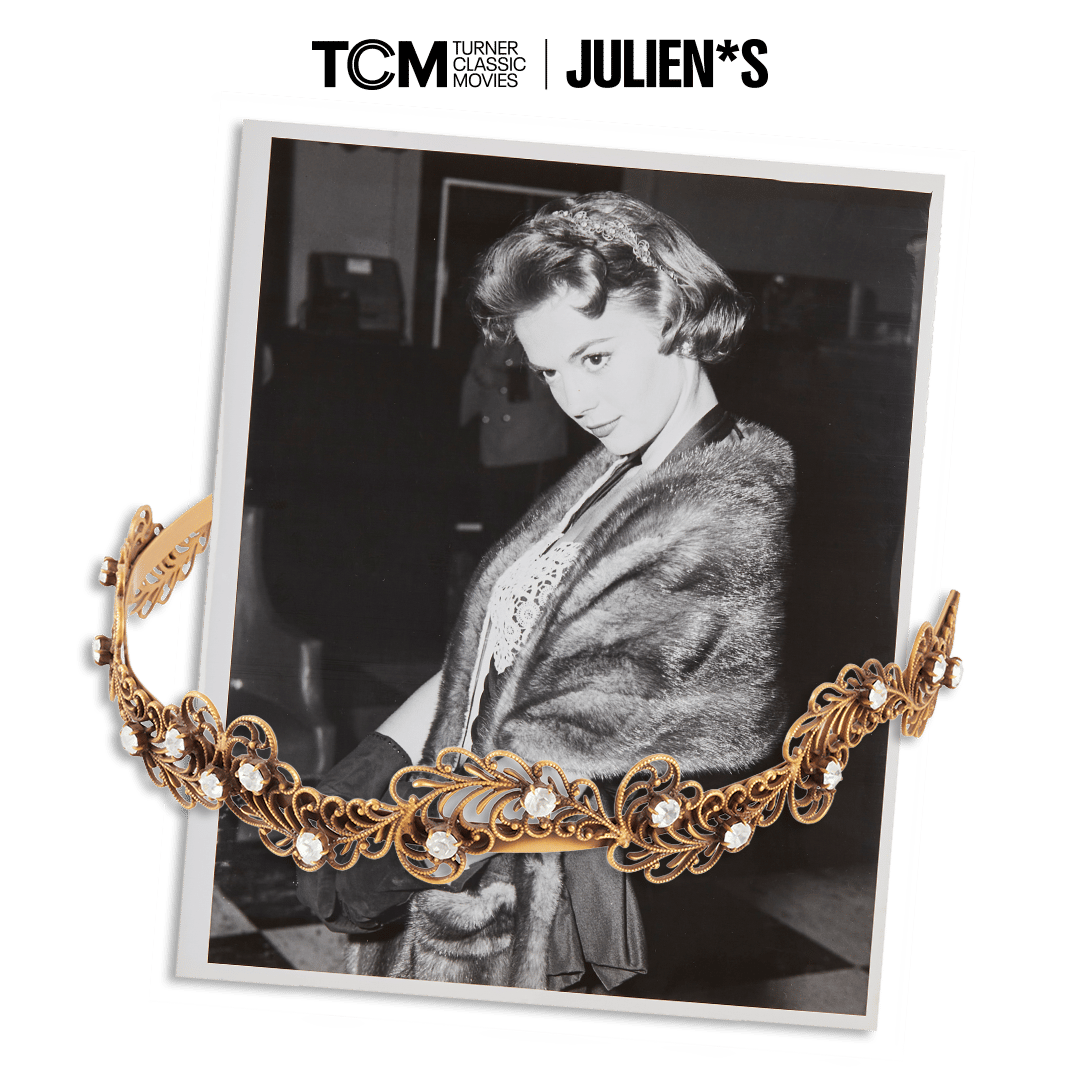 Black and white photo of a woman in a fur stole, with an ornate gold and jeweled tiara in the foreground.