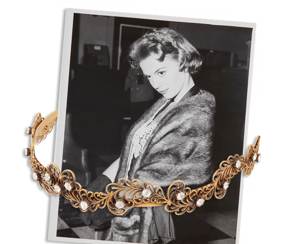 Black and white photo of a woman in a fur stole, with an ornate gold and jeweled tiara in the foreground.