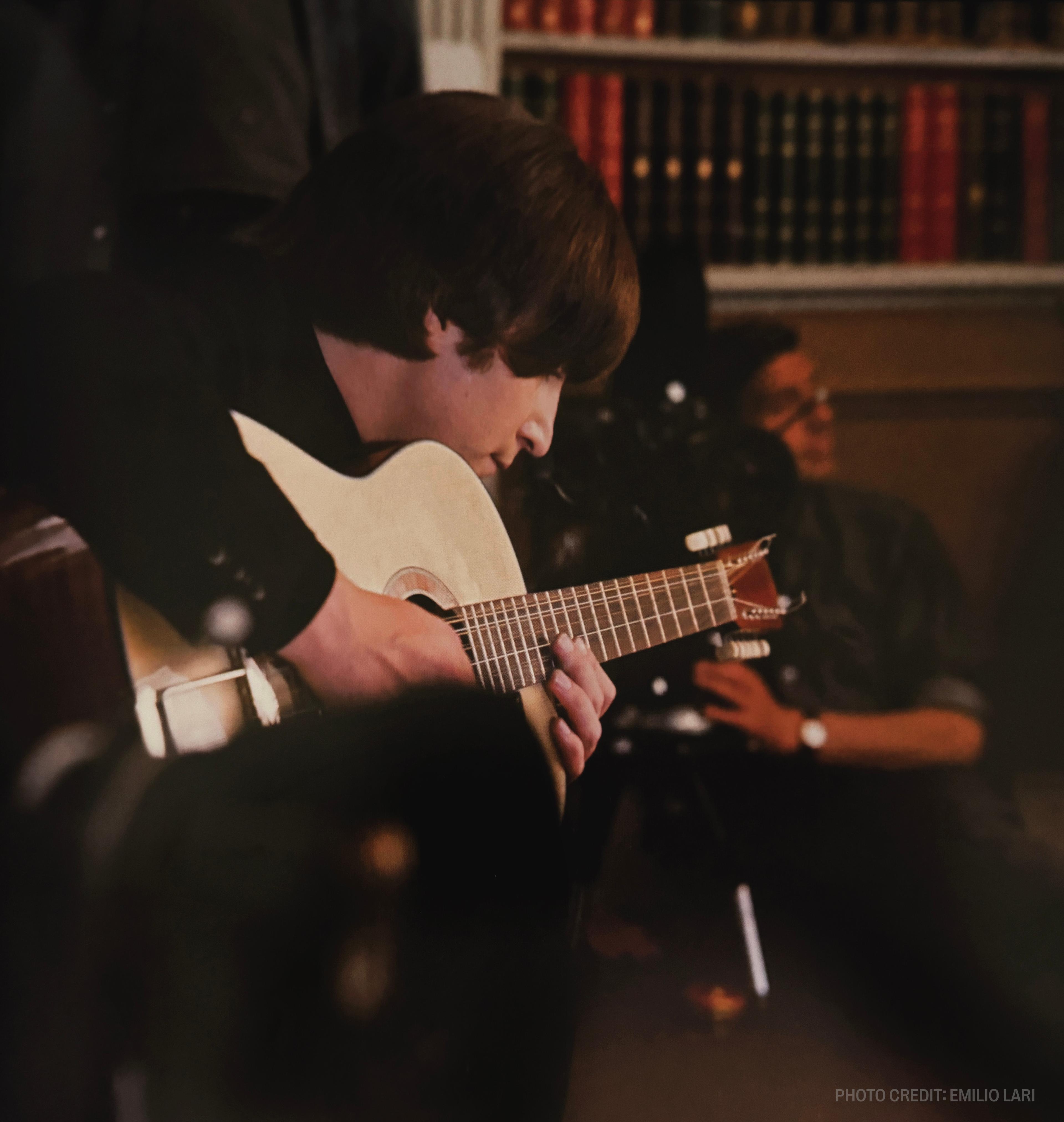a man is playing a guitar in front of a bookshelf