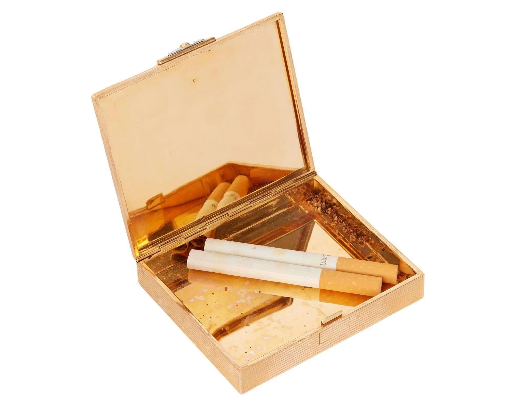 Open gold cigarette case with two cigarettes and tobacco residue.